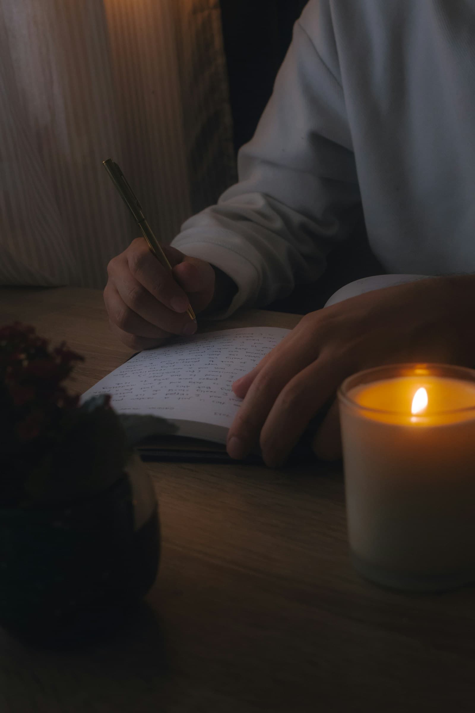 A person writing in a notebook beside a lit candle
