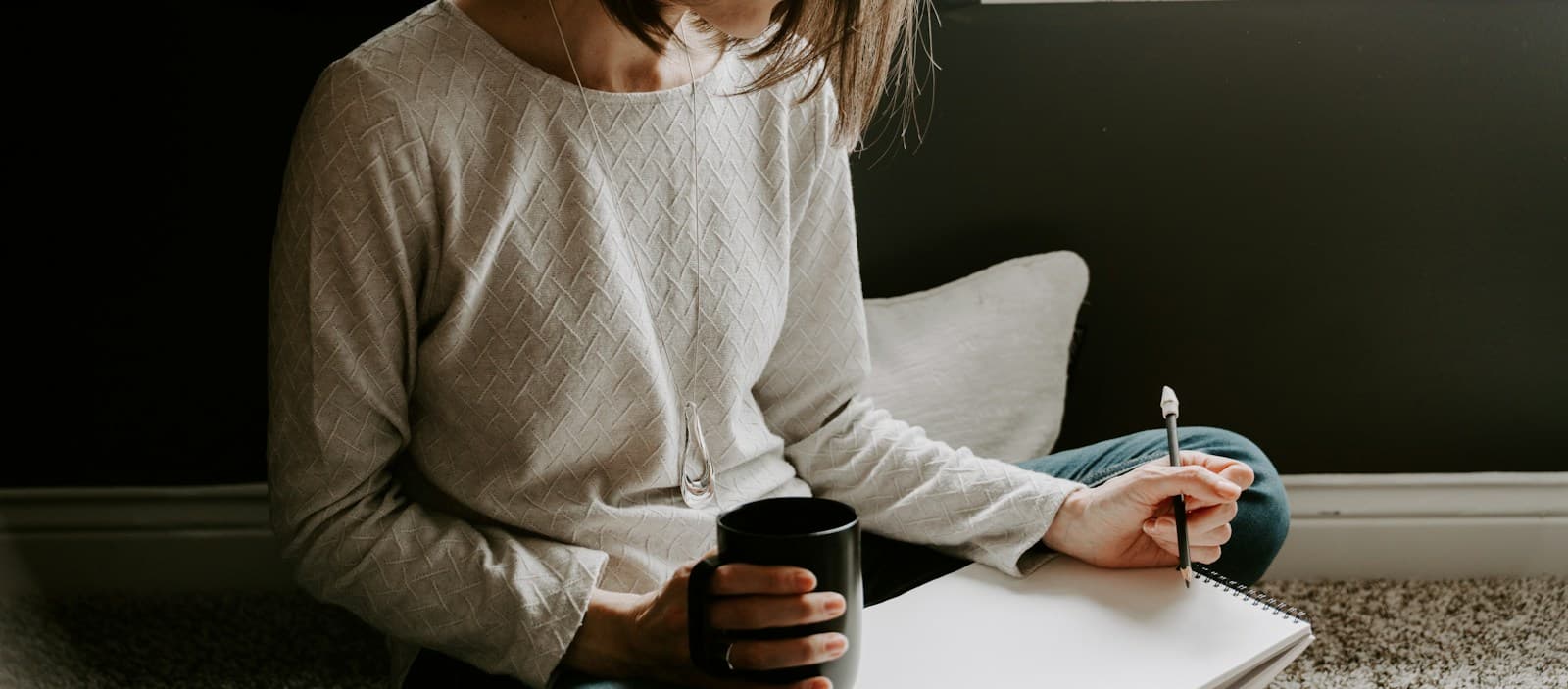 A person holding a mug while writing in an open notebook
