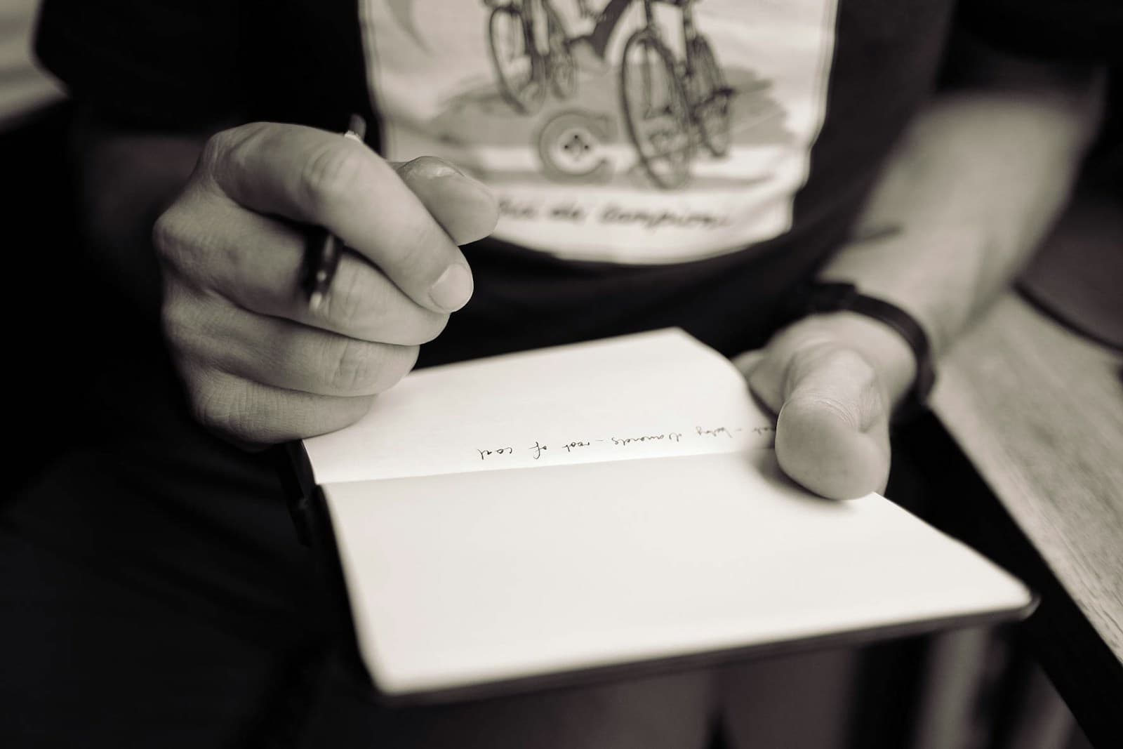 A close-up of someone writing the first lines in an open notebook